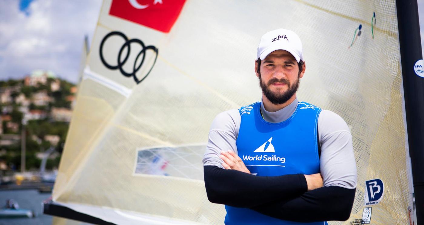 Portrait of Alican Kaynar in front of his Finn sail